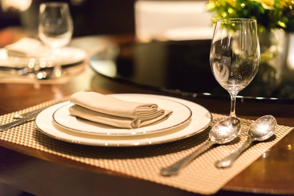 Close up of empty glasses in a restaurant with a blurred background and a plate with a napkin and spoon on the table.